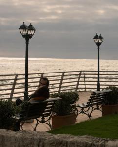 a man sitting on a bench next to the ocean at Vila Gale Ericeira in Ericeira