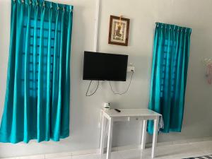 Una habitación con cortinas azules y un televisor y una mesa. en Al Bayt Roomstay Kaki Gunung Jerai, en Kampung Gurun