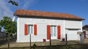 a white house with red doors and a fence at Les tilleuls in Soustons