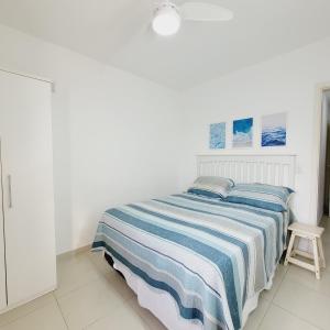 a white bedroom with a bed with a blue and white striped blanket at Paraiso no Guarujá Enseada - Piscina - Ar Condicionado - WIFI - Garagem in Guarujá