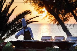 a chef preparing food on a grill in front of the ocean at Sani Club in Sani Beach