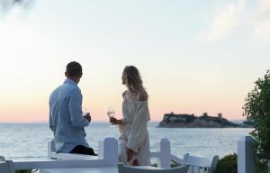 a man and woman standing next to the ocean holding wine glasses at Sani Club in Sani Beach