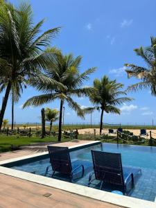 une piscine avec deux chaises et des palmiers dans l'établissement Casa beira mar - Carneiros (30’ de carro), à Sirinhaém