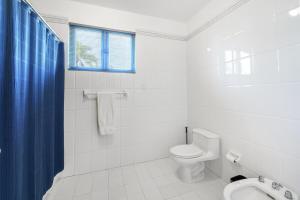 a white bathroom with a toilet and a blue shower curtain at Quaint villa Beach access Elina in Sabana +53 photos