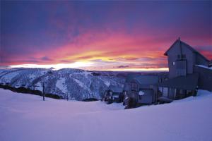 a building in the snow with a sunset in the background at Gotcha in Mount Hotham