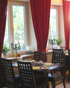 una sala da pranzo con tavolo, sedie e tende rosse di Hotel Biederstein am Englischen Garten a Monaco