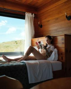 a woman sitting on a bed reading a book at É diferente, descubra por quê in Urubici