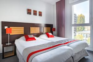 um quarto com 2 camas com almofadas vermelhas e uma janela em Lagrange Apart’Hotel Strasbourg Wilson em Estrasburgo