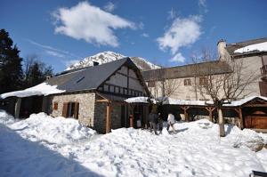 deux personnes debout dans la neige devant un bâtiment dans l'établissement Gîtes Au Chant des Marmites, à Saint-Lary-Soulan