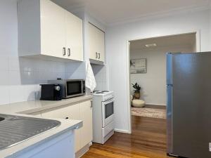 Una cocina con gabinetes blancos y un refrigerador de acero inoxidable. en Casa Solé - Calm 1BR Escape by Towradgi Beach, en Towradgi