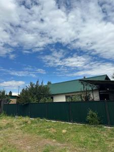 a house with a green fence and a cloudy sky at Taizhan in Ak-Bulun