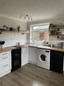 een keuken met een spoelbak en een wasmachine bij Barley Break - Beach Cottage in Lessingham