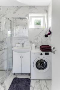 a white bathroom with a washing machine and a sink at Vila Naktižiedė in Šventoji