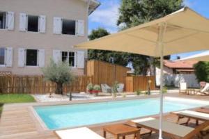 a swimming pool with an umbrella and a house at Hôtel Le Grain de Sable in Arès