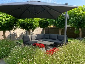 un divano sotto un ombrellone in un giardino fiorito di Crea Els a Westerlo
