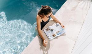 a woman sitting by a swimming pool reading a newspaper at Finns at Old Bar in Old Bar