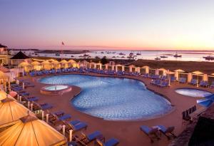 a resort pool with chairs and umbrellas and the ocean at Chatham Bars Inn in Chatham