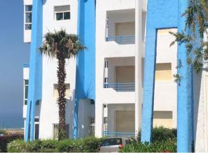 a blue building with palm trees in front of it at Appartement avec piscine in Asilah