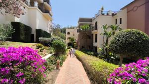 two people walking down a path through a garden with pink flowers at Las Jacarandas Penthouse with Stunning Views & Private Rooftop in Benahavís