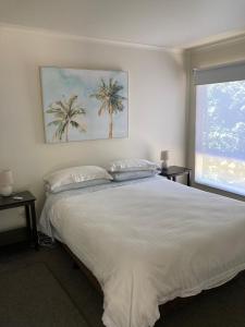 a bedroom with a large white bed with two palm trees at Waterfall Cottage in Rosebud
