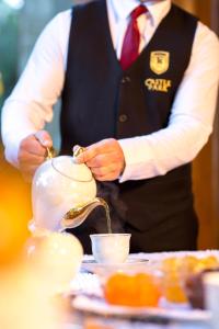 un hombre está vertiendo té en una tetera en Hotel Castle Park, en Berat