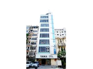 YAMA HOTEL & ROOFTOP BAR في يانغون: مبنى طويل وبه سيارات متوقفة أمامه