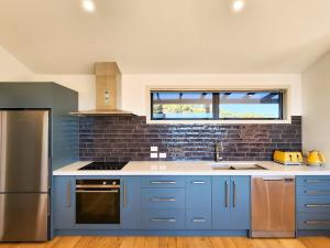 a kitchen with blue cabinets and a brick wall at The Barn Hot Water Beach in Hotwater Beach