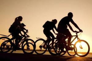 three people riding bikes on the beach at sunset at De Clinique Hotel in Pangkor