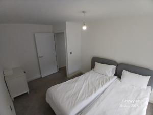 un dormitorio con una cama con sábanas y almohadas blancas en Hornchurch House - Romford, en Harold Wood