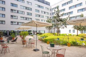 a patio with tables and chairs and umbrellas in front of a building at Hyatt Place Paris Charles de Gaulle Airport in Roissy-en-France