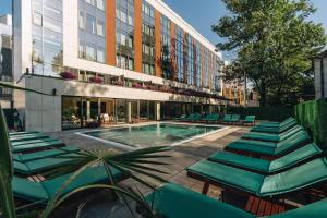 a pool with green lounge chairs and a building at Hotel Tonanti in Vrnjačka Banja