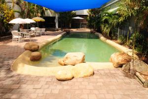 uma piscina com pedras, uma mesa e um guarda-sol em Hotel Allen em Townsville