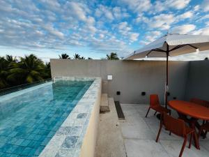 a swimming pool with a table and an umbrella at Villa Mutum - Triplex na Rota Ecológica dos Milagres Praia do Patacho in Pôrto de Pedras