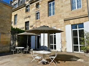 two tables and chairs with an umbrella in front of a building at DE L'ART À LA MANIÈRE - Chambre d'Hôtes de Charme - 2 Suites Haut de Gamme - Idéal Couple & Famille - Piscine - Terrasse - Calme - 15min Saint-Émilion - EXPÉRIENCE Restauration d'Oeuvre d'Art in Branne