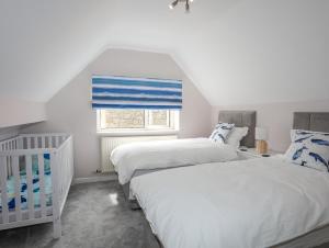 two beds in a bedroom with a crib and a window at Swn Y Mor in Benllech