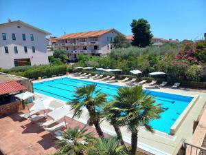 a large swimming pool with chairs and palm trees at Green Sporting Club Hotel in Alghero
