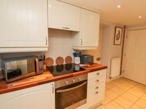 eine Küche mit weißen Schränken und einer Mikrowelle in der Unterkunft Woodcutters Cottage in Haltwhistle + 11 Fotos