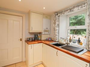 eine Küche mit weißen Schränken und einer Spüle und einem Fenster in der Unterkunft Woodcutters Cottage in Haltwhistle