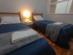 two beds in a room with a lamp on a table at Na Cidade Baixa, perto de tudo - UFRGS, Santa Casa, Parques, Orla in Porto Alegre