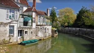 a green boat in a river between two buildings at La maison papillon in Tonnerre