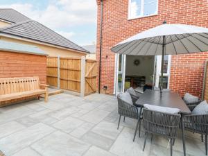 a patio with a table with an umbrella and a bench at Pine Cottage in Beccles