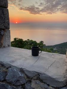 a coffee cup sitting on a ledge with the sunset at Shiro - traditional stone villa in Agriliá +11 photos