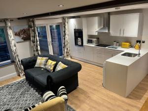 a living room with a black couch and a kitchen at Little Sycamore in Lyminge