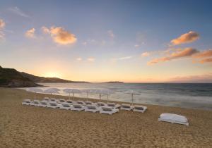 a group of white chairs and umbrellas on a beach at Mykonos Bay Resort & Villas in Mikonos