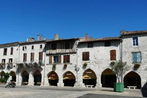 an old stone building with arches in a street at Joli petit appartement in Eymet