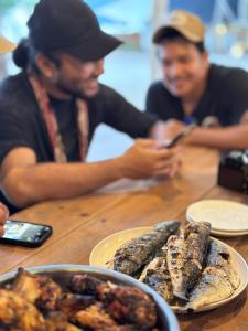 Due uomini seduti a un tavolo con piatti di cibo di Juita Glamping Perhentian island a Isole Perhentian
