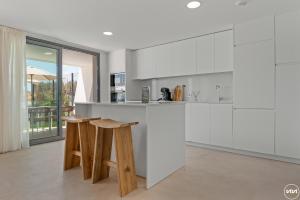 a kitchen with white cabinets and wooden stools at ViVi Homes - Marisol Pool, Sauna, Gym, Spa & Beach in Mijas Costa +41 photos