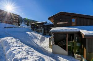 a building covered in snow with the sun behind it at Résidence Backgammon - LE BACKGAMMON MAE-3560 in Les Coches