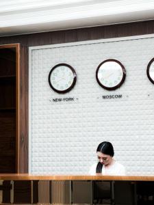 a woman sitting in front of a wall with clocks at Jasmine in Taraz