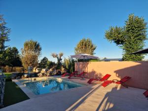 a swimming pool with red chairs and an umbrella at La grange des vignes in Pomport